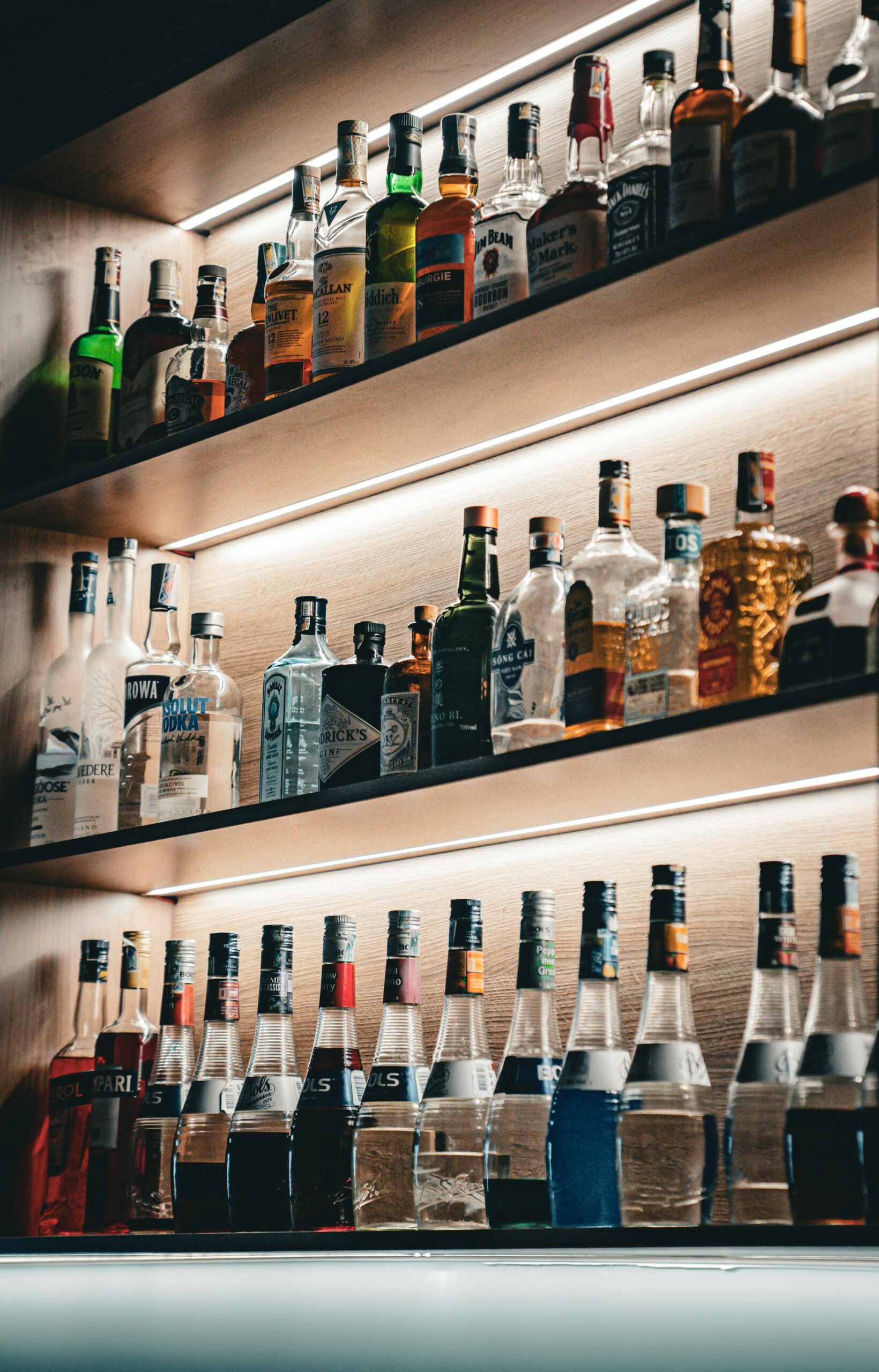 An array of bottles neatly arranged on backlit shelves.